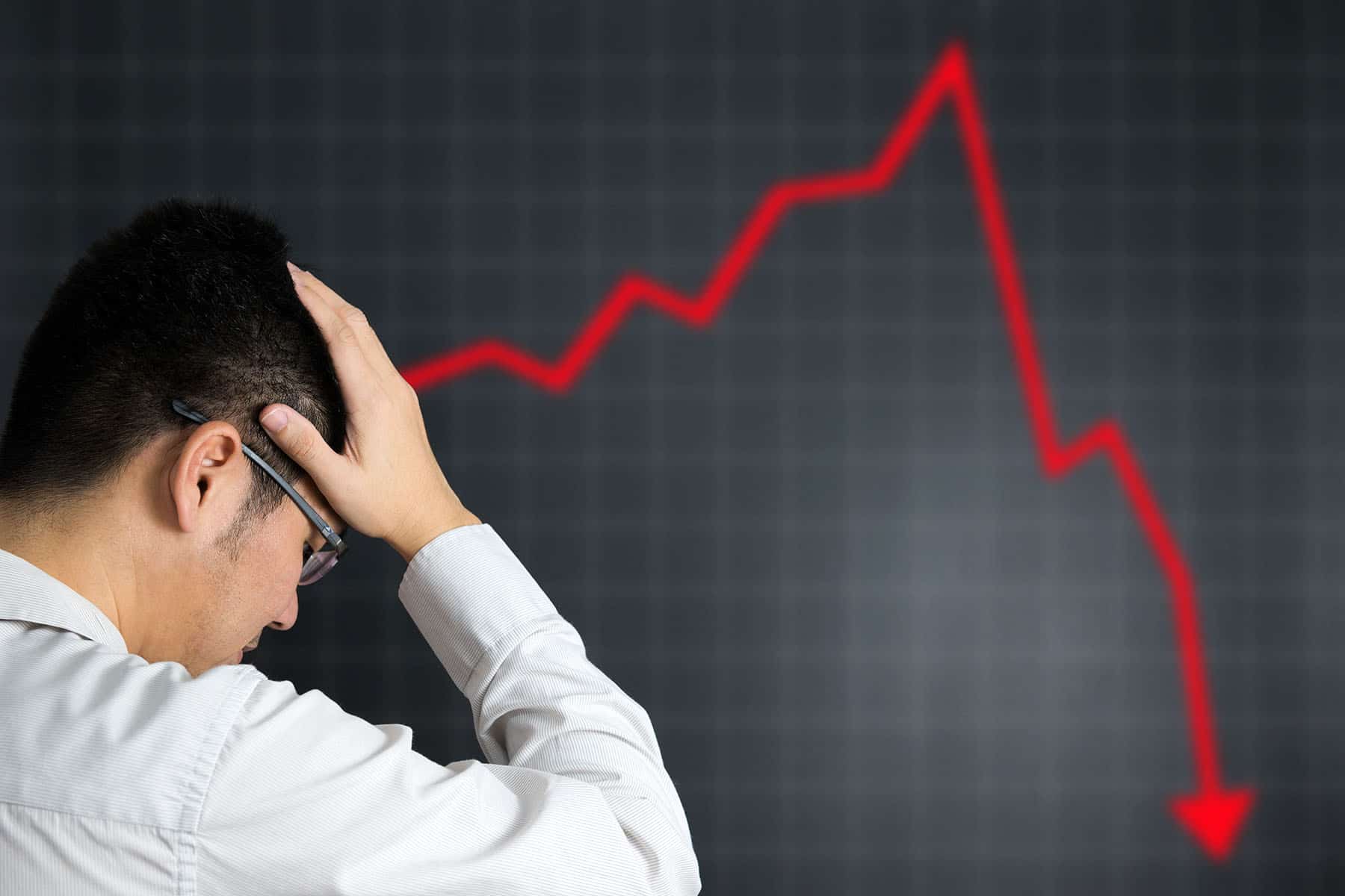 Man holding head in front of image of stock value plummeting